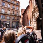Bus cabriolet rouge CityTour Toulouse devant l'Hôtel d'Assezat avec touristes à bord